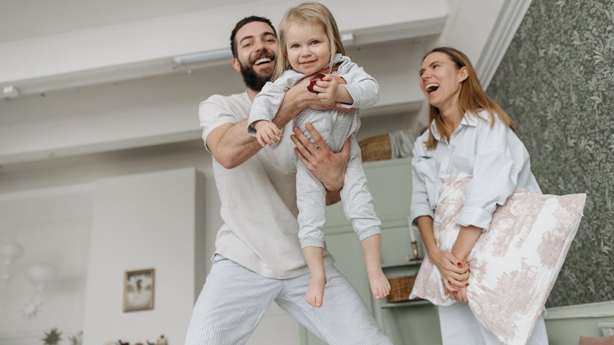 Cheerful family with parents playing and lifting child in a cozy living room.